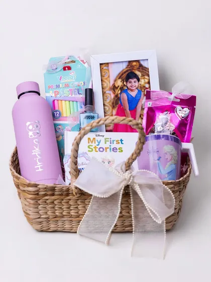 Creating a basket full of joy for a little one's birthday. This 'Frozen' themed hamper includes a personalized water bottle, a storybook, art supplies, and a framed photo, making it a magical and personal gift.