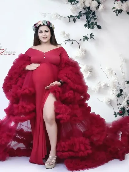 A full-length portrait of an expectant mother in a stunning red ruffled gown, set against a wall of white and red roses. This look is perfect for a romantic and glamorous maternity session.