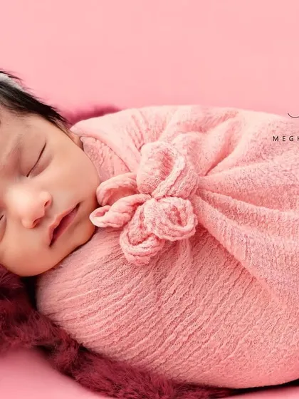 This baby is dreaming sweetly, wrapped in a soft pink swaddle with a floral headband. The monochrome pink setup is gentle and classic.