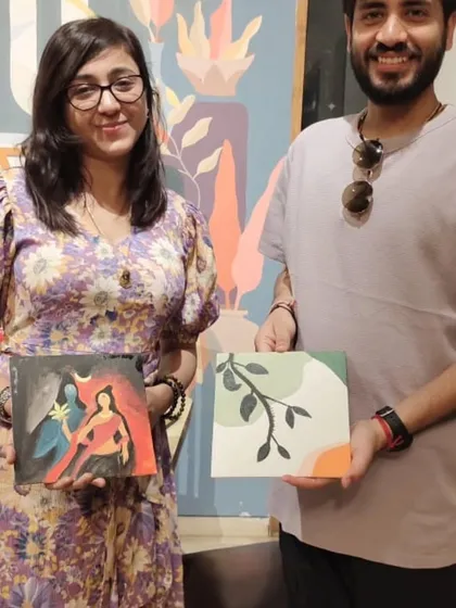 A couple displays their finished canvases. One features a divine depiction of Shiva and Parvati, while the other is a minimalist leaf design, showing the range of styles explored in our workshops.