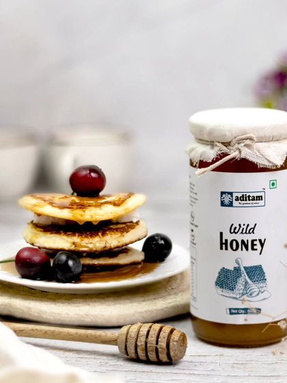 A jar of wild honey is styled next to a delicious stack of pancakes topped with fresh berries. This appetizing breakfast scene creates a sweet and wholesome story for the product.