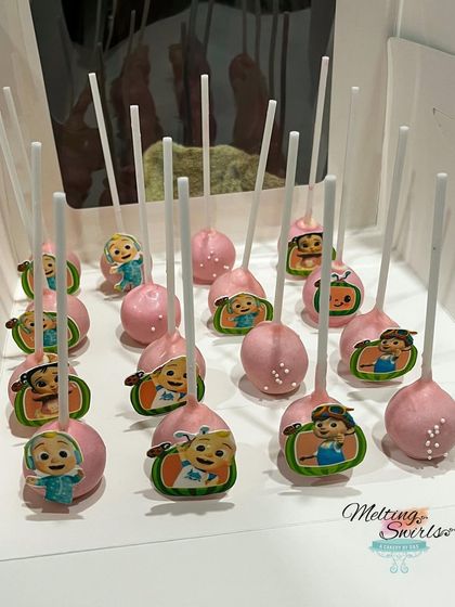 A box of our Cocomelon cake pops, all ready for the party. Each pink cake pop is decorated with an edible image of a different character from the popular children's show.