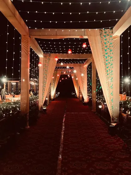 A simple yet effective entrance design using draped fabric and hanging fairy lights to create an elegant and understated walkway.