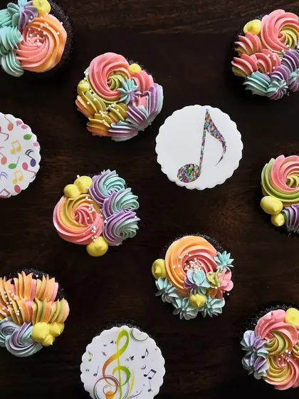 A splash of colour to brighten anyone's day. This set features vibrant, rainbow-coloured buttercream swirls on chocolate cupcakes, alongside custom edible toppers with a cheerful musical note theme. It's pure happiness in a box.
