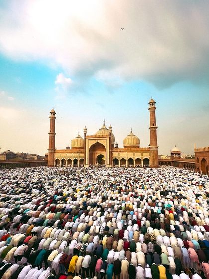 The grand facade of Jama Masjid stands against a beautiful sky as a sea of people pray in its courtyard.