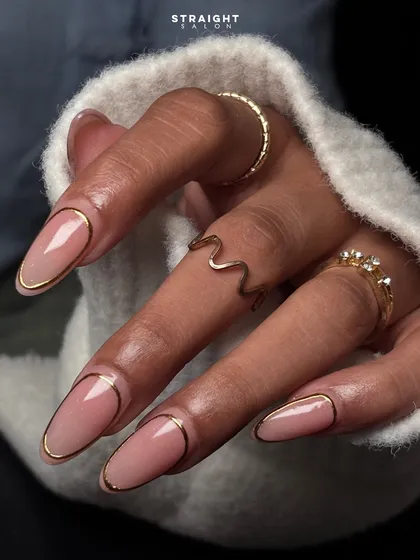 Understated elegance with a touch of gold. This minimalist design features a clean nude base on long oval nails, framed with a delicate, hand-painted gold outline for a chic and modern look.