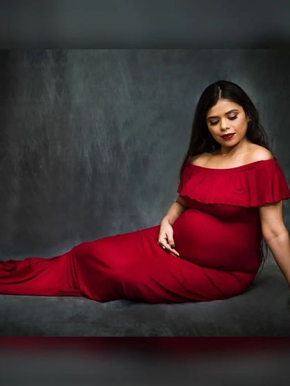 A simple yet powerful seated portrait against a textured dark grey backdrop. The focus here is entirely on the mother-to-be, with the vibrant red of the gown providing a beautiful contrast.