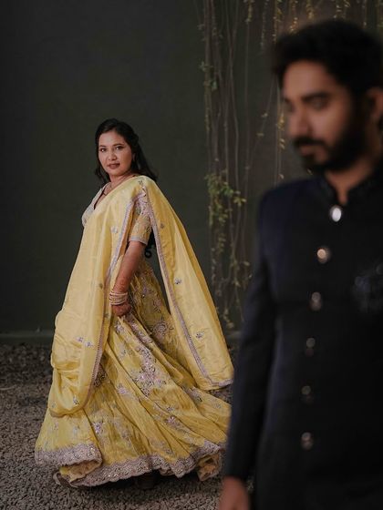 An artistic shot with the groom in the foreground, and the bride in her flowing yellow lehenga behind him, creating a beautiful sense of depth.