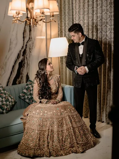 A stylish portrait of the couple in a modern, luxurious room. The bride is seated while the groom stands, creating a dynamic and fashionable composition.