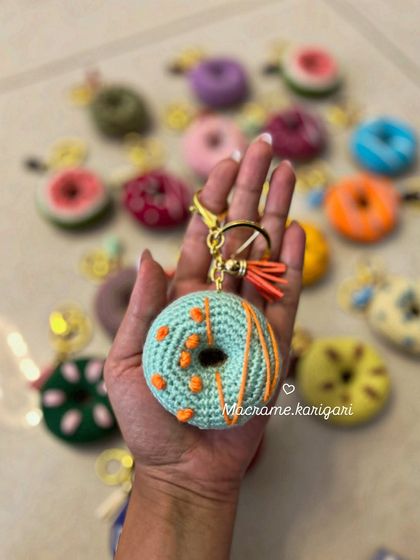 Holding up a mint-chocolate chip inspired donut keychain. Each one comes with a high-quality clasp and a small tassel for extra flair.