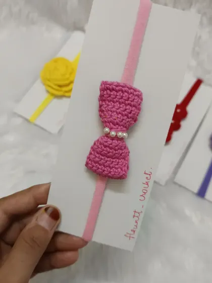 A sweet pink bow with pearl details on a light pink nylon headband, perfect for a little girl.