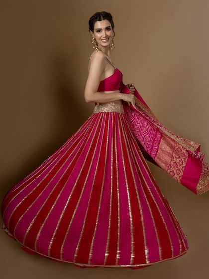 A model twirls in a red and pink striped lehenga, showing off its beautiful flare and the rich texture of the fabric.