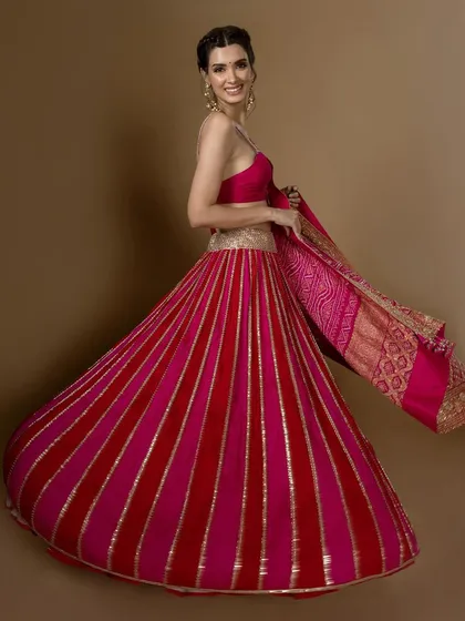 A model twirls in a red and pink striped lehenga, showing off its beautiful flare and the rich texture of the fabric.