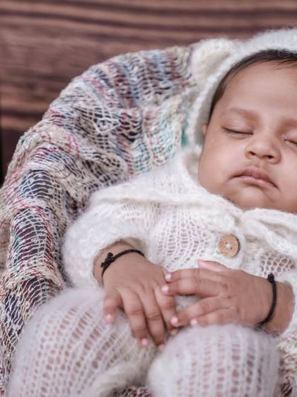 A close-up of the baby in the vintage setup, nestled in a basket with a stack of classic books in the background.