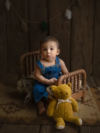The cutest pout. This 8-month-old is sitting up on his own next to a tiny bed and his teddy bear, a perfect way to document a new skill in a rustic-themed milestone shoot.