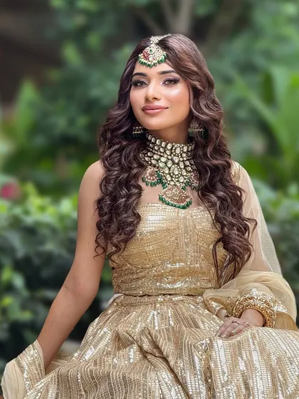 A beautiful outdoor shot of a bride in a golden lehenga. The makeup is soft and natural, perfect for daytime.