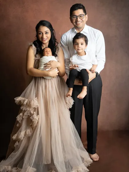 A beautiful portrait of a family of four. The mother is holding the newborn while the father stands proudly with their older son.