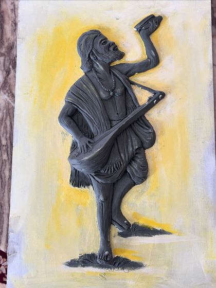 The clay sculpture of Kanaka Dasa is complete and set against a simple painted background, showing the raw texture of the artwork before final touches.