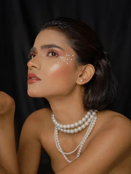 An upward-looking beauty portrait that showcases the model's makeup and pearl necklace. The lighting creates a soft glow on her skin, enhancing the overall ethereal feel.