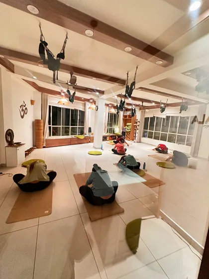 A view from the doorway of a class settling into a seated forward fold, the evening light creating a peaceful mood.