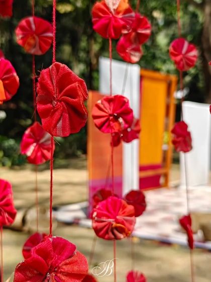Delicate red flowers crafted from scrap fabric hang as a curtain, with a personalized wedding stage visible in the background. This showcases how upcycled elements can be used to create texture and depth.