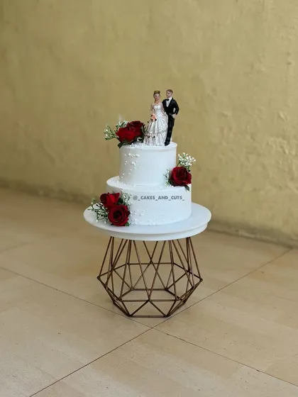 A simple and sweet two-tier wedding cake with a classic bride and groom topper and fresh red roses. It's a timeless design for a beautiful celebration.