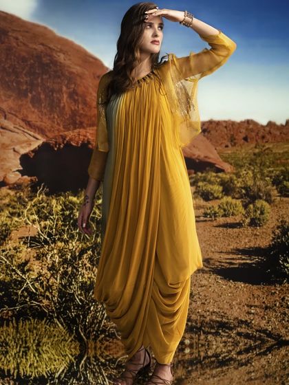 Here, a desert landscape is projected behind the model. The lighting is designed to be warm and directional, as if from a setting sun, creating a dramatic and flowing silhouette.