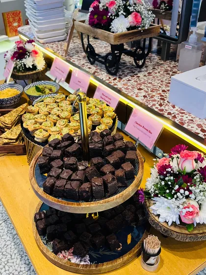 We believe presentation is key. This image shows our two-tiered wooden platter of brownie bites, surrounded by fresh flowers, creating an inviting and high-end feel for the corporate event.
