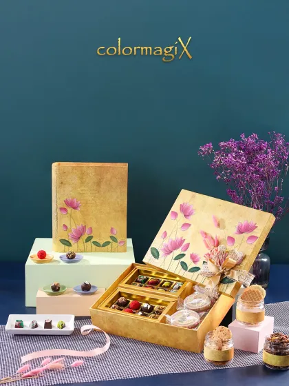 A luxurious golden "book box" hamper, hand-painted with a beautiful lotus design. It opens to reveal a decadent assortment of chocolates and dessert jars.