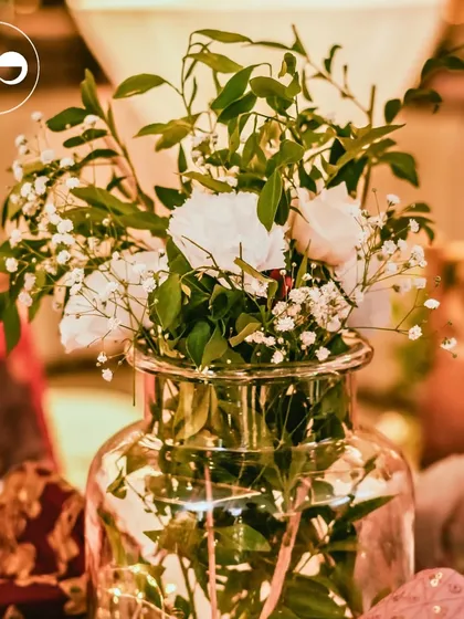 A simple glass vase with white carnations and fairy lights inside, creating a magical and warm centerpiece for an evening ceremony.