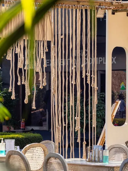 The seating area of our pop-up cafe design for Cafe Tesu at the India Art Fair. This view highlights the boho-chic aesthetic, featuring macrame curtains, cane-back chairs, and a natural color palette that creates a relaxed and stylish space.