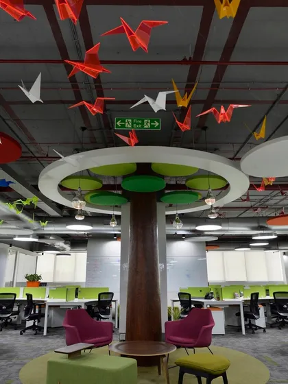 The "learn under the tree" collaboration area. A stylized tree structure with colorful origami birds hanging from the ceiling creates a whimsical, nature-inspired meeting spot in the open office.