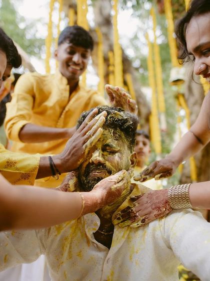 The groom getting playfully smeared with turmeric paste by his family and friends during the Haldi ceremony.