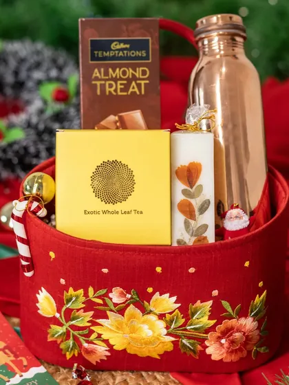 This embroidered red basket makes for a luxurious Christmas gift. It's filled with a copper bottle, a box of whole leaf tea, a floral-pressed candle, and Cadbury Temptations chocolate.