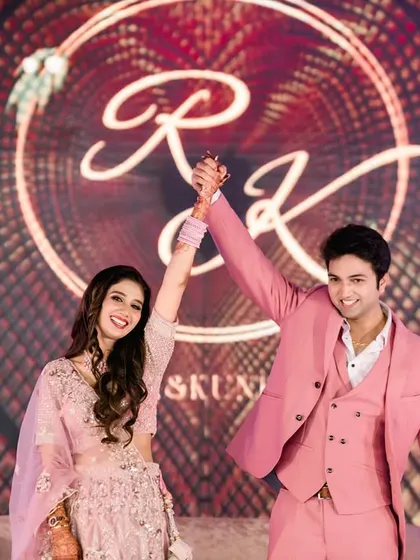 A triumphant moment as the newly engaged couple raises their hands in celebration. Their joy is palpable, perfectly framed by their custom monogram and the vibrant floral decor of the stage.