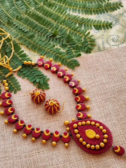 A beautiful teardrop-shaped necklace in maroon and gold, with intricate work on the pendant. It comes with a cute little hanging jhumka.