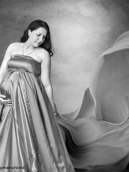 The same elegance of a flowing gown, captured in timeless black and white. This artistic choice removes all distractions, focusing on the texture of the fabric, the soft light, and the mother's gentle pose.
