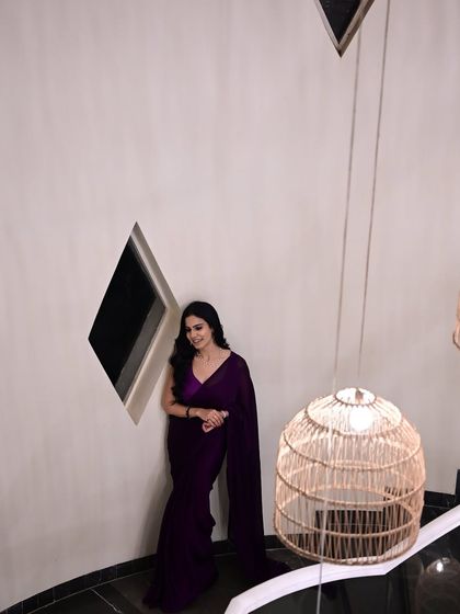 A high-angle shot of me in a deep purple saree, leaning against a wall. This creative angle highlights the modern architecture and the sleek saree.