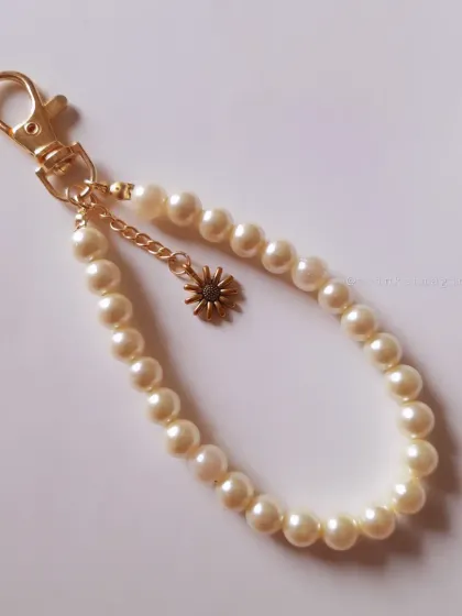 A simple and elegant pearl beaded keychain with a single sun charm. It's a timeless accessory that adds a touch of class to your keys or bag.