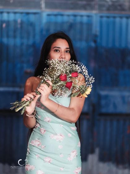 A playful and charming portrait, peeking over a bouquet of flowers. The vibrant blue background makes the colors of the flowers pop.