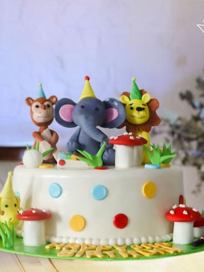 A jungle party in full swing. This cake features a lion, elephant, and monkey wearing party hats, surrounded by colorful polka dots and mushrooms.