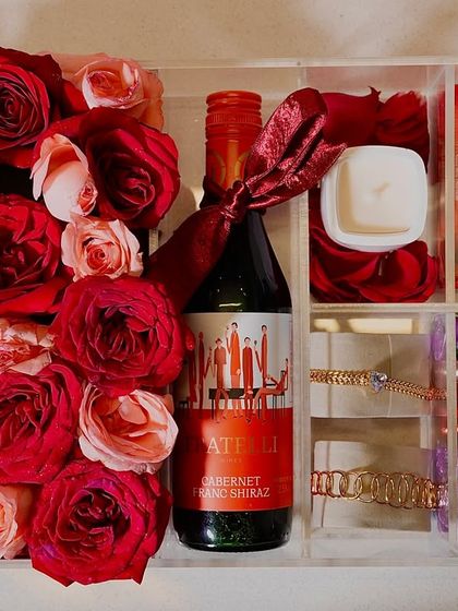 A top-down view of our "Love Affair 2.0" hamper, showcasing the curated selection of red roses, a bottle of wine, a scented candle, bracelets, and colorful chocolates, all nestled in a clear acrylic box.
