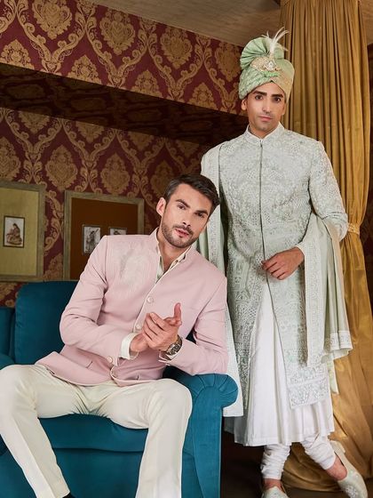A groom in a light green sherwani stands with his best man, who is dressed in a complementary pink bandhgala. This is how I create visual harmony for your most important photos.