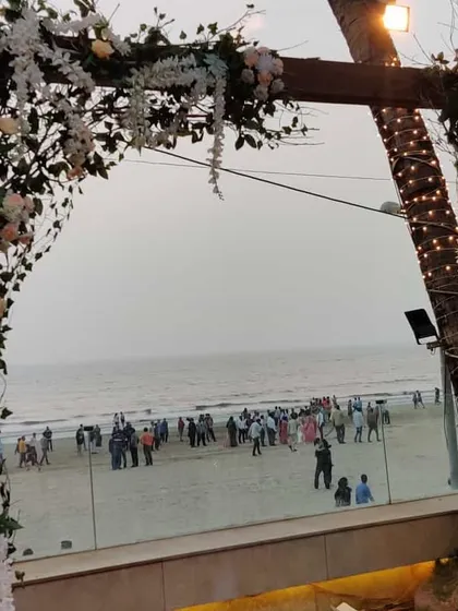 A rustic wooden arch decorated with white and blush flowers frames the ocean view perfectly. This simple yet elegant structure served as a beautiful photo point and entrance for a beachside engagement ceremony.
