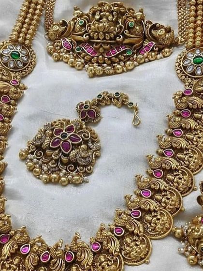 This close-up shows the detail of a traditional temple jewellery haaram. The piece features intricate carvings of deities and is studded with kemp stones.