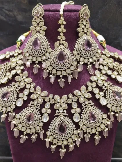 This elaborate silver-toned necklace set features intricate floral motifs with pastel purple stones. It's a unique choice for a reception or engagement and is available to rent as a complete set with earrings and maang tikka.