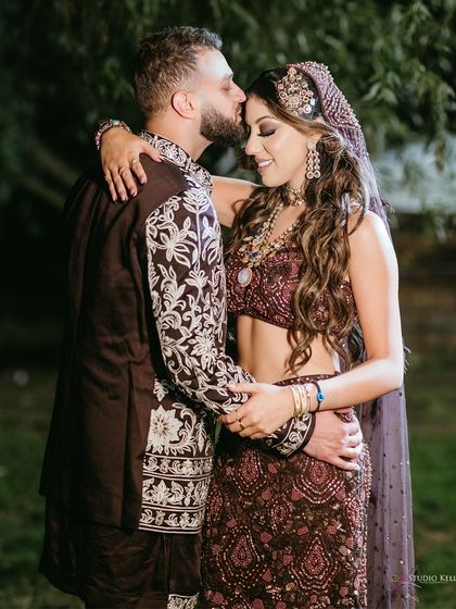 A tender moment between the couple during their London wedding reception, the groom kissing the bride's forehead as they embrace.
