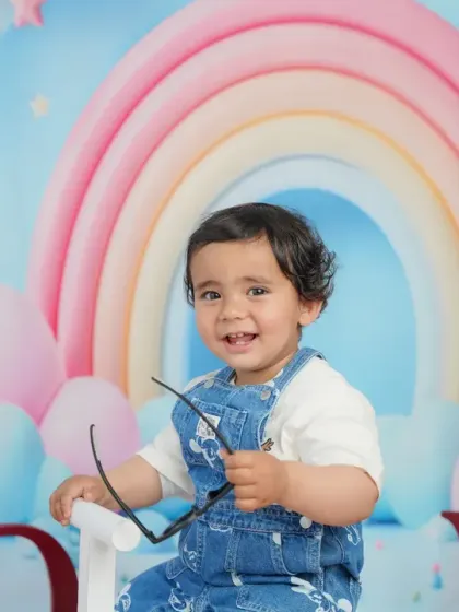 This little one is ready for his close-up, holding a pair of sunglasses and flashing a charming smile during his rainbow-themed shoot.
