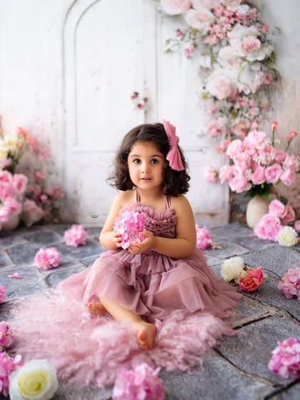 A sweet floor portrait of the birthday girl in a dusty rose dress, surrounded by pink flowers.