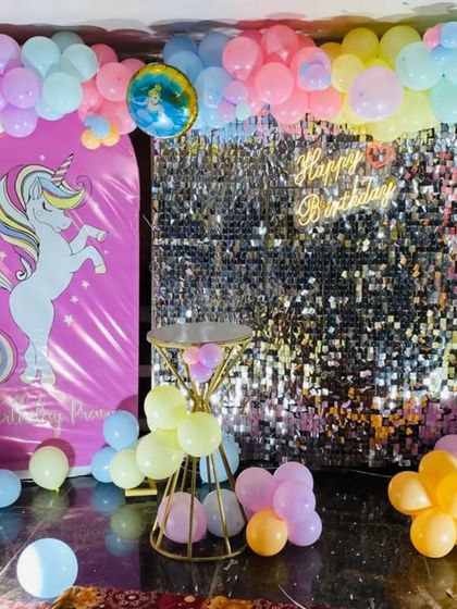 A magical unicorn-themed birthday setup. This decoration combines a unicorn backdrop with a silver shimmer wall, a light-up number "1", and a pastel balloon arrangement.